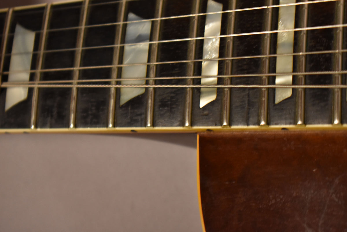 Close-up of the dark fretboard with trapezoid mother-of-pearl inlays, frets, and strings, with a hint of the sunburst body.