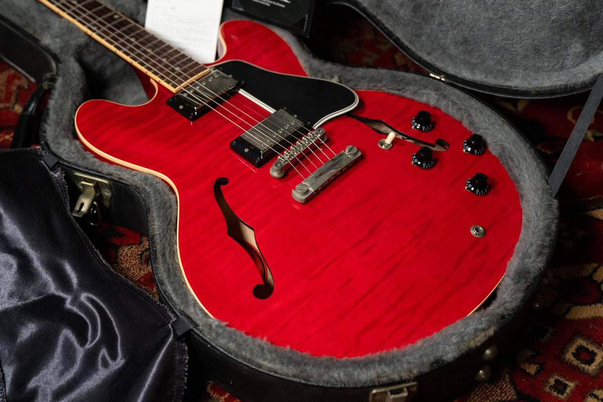 Cherry red flamed maple semi-hollow guitar in its open hard case, showing the body, f-holes, pickups, and control knobs.
