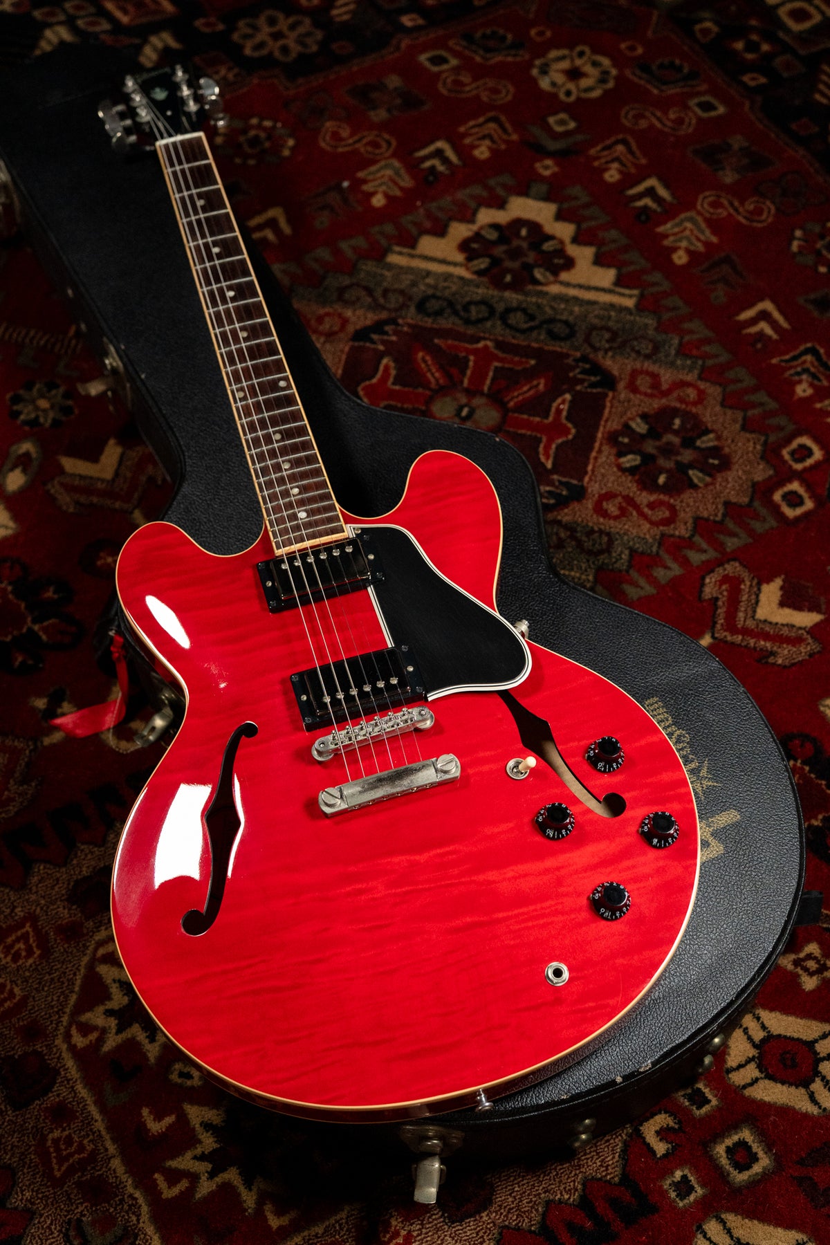 Cherry red flamed maple ES-335, angled in its open black case, shows two humbuckers, four black knobs, and a worn bridge.