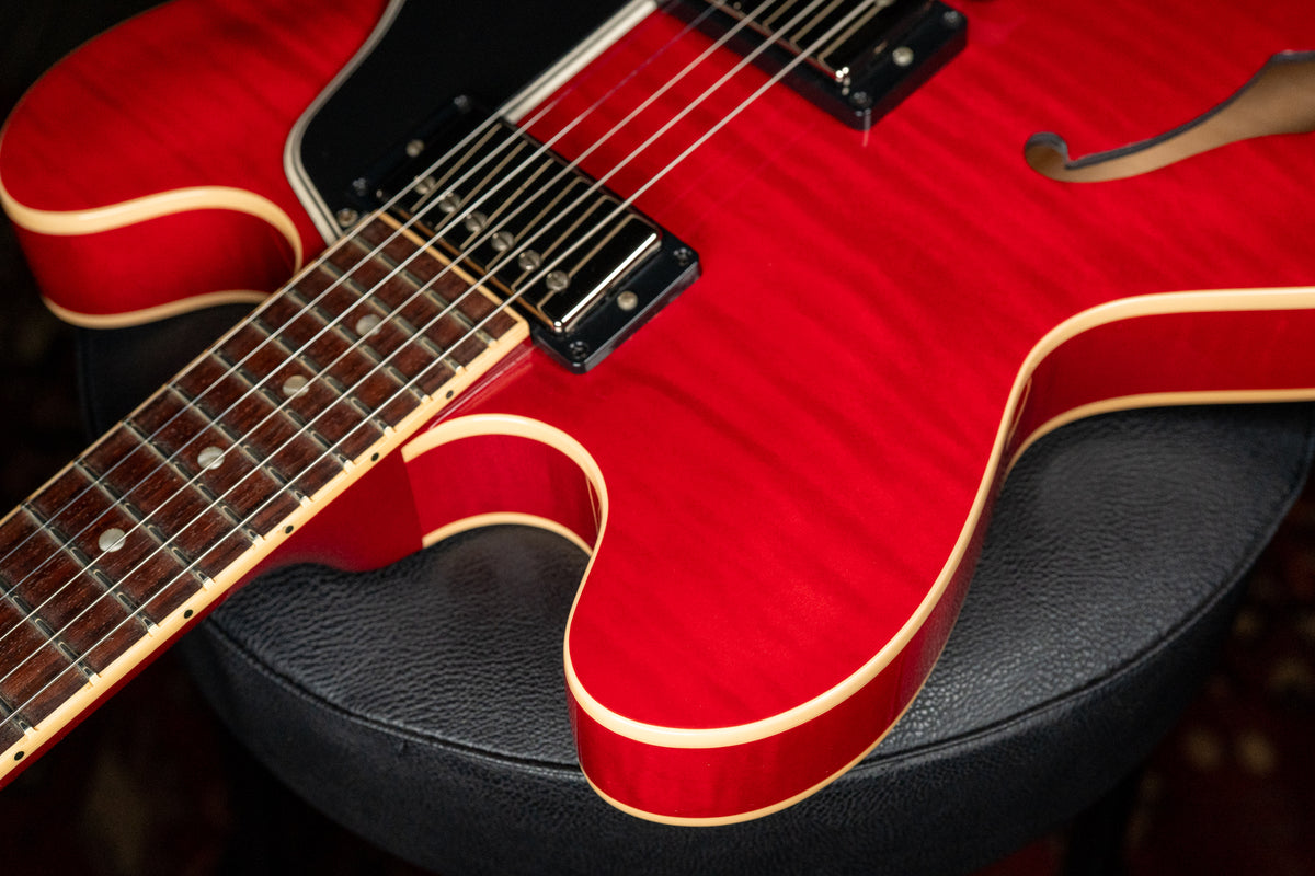 Close-up of a cherry red flamed maple guitar body with cream binding, black pickguard, and two black humbucker pickups.