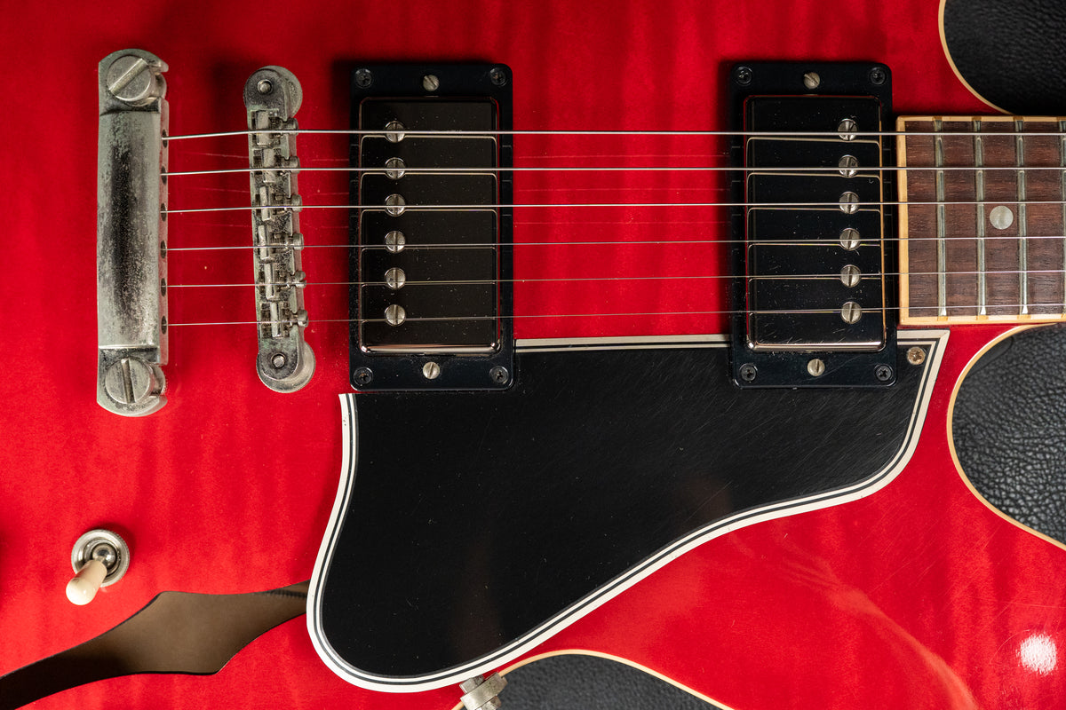 Close-up of the cherry red flamed maple body, showing the bridge, two humbuckers, black pickguard, and lower F-hole.