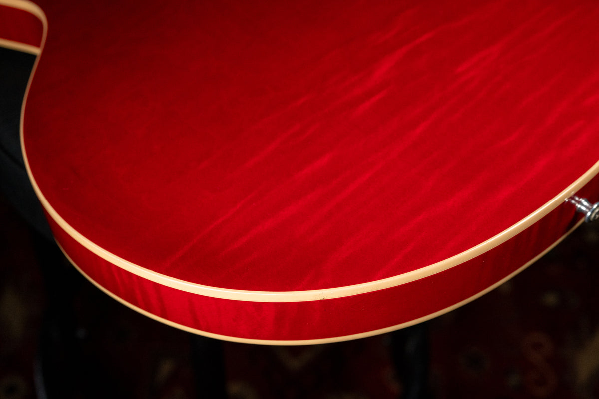 The lower bout of a cherry red flamed maple guitar body, showing cream binding and a chrome strap button.