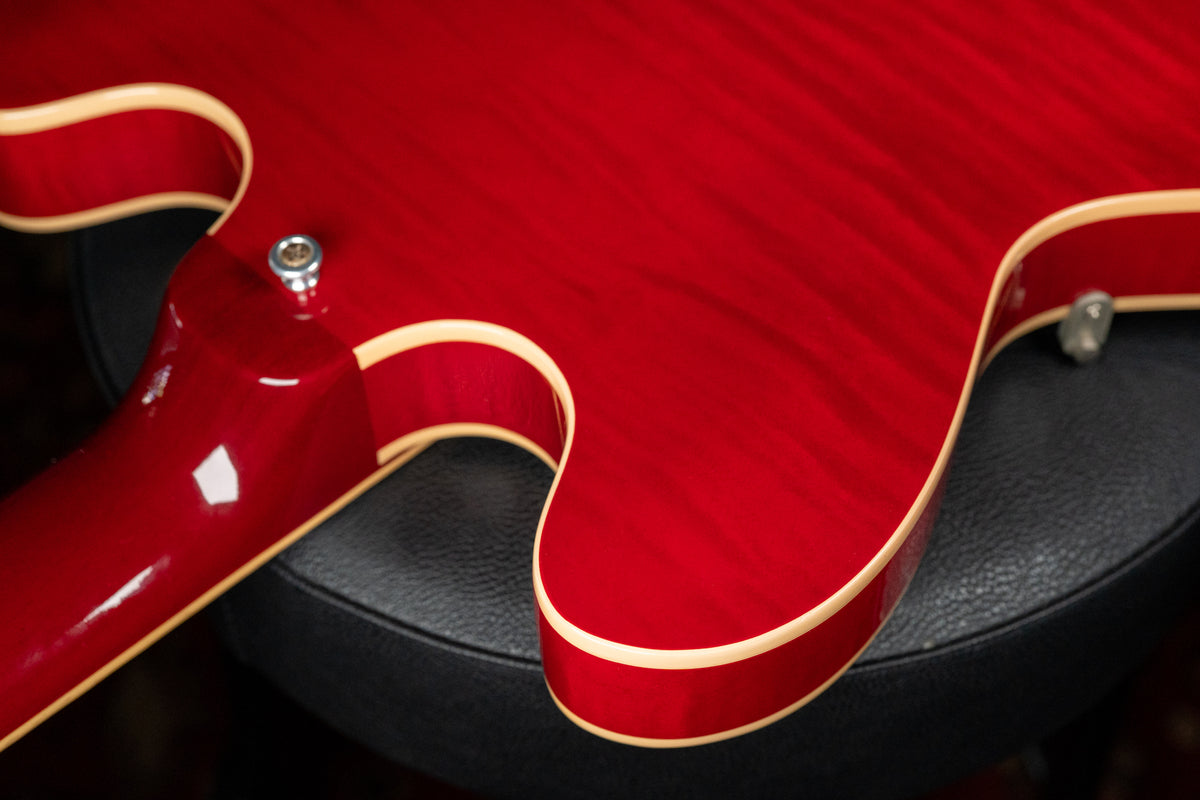 The guitar's cherry red flamed maple body, with cream binding, is seen from the back, showing the neck joint and strap button.