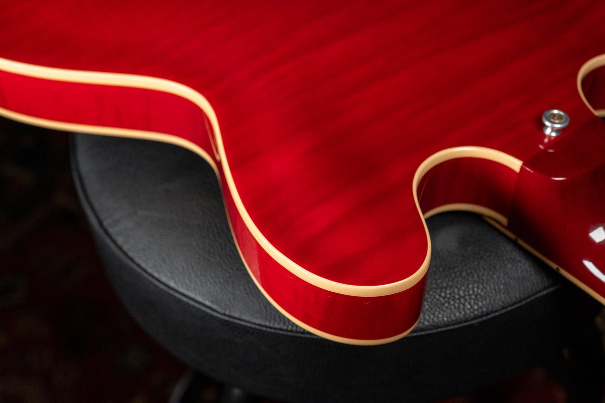 Close-up of the guitar's lower bout, showing the cherry red flamed maple top, cream binding, and a chrome strap button.