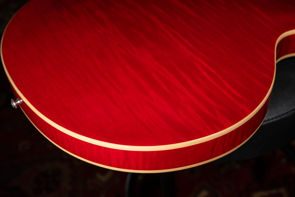 Close-up of the guitar's lower bout, showing the cherry red flamed maple top, cream binding, and a chrome strap button.