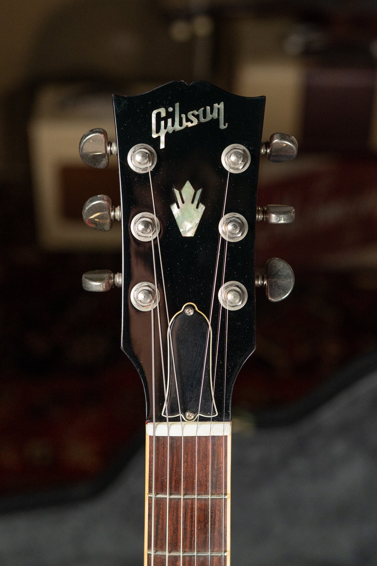 Close-up of a glossy black headstock with mother-of-pearl inlay, six chrome tuners, and the top of a dark rosewood fretboard.