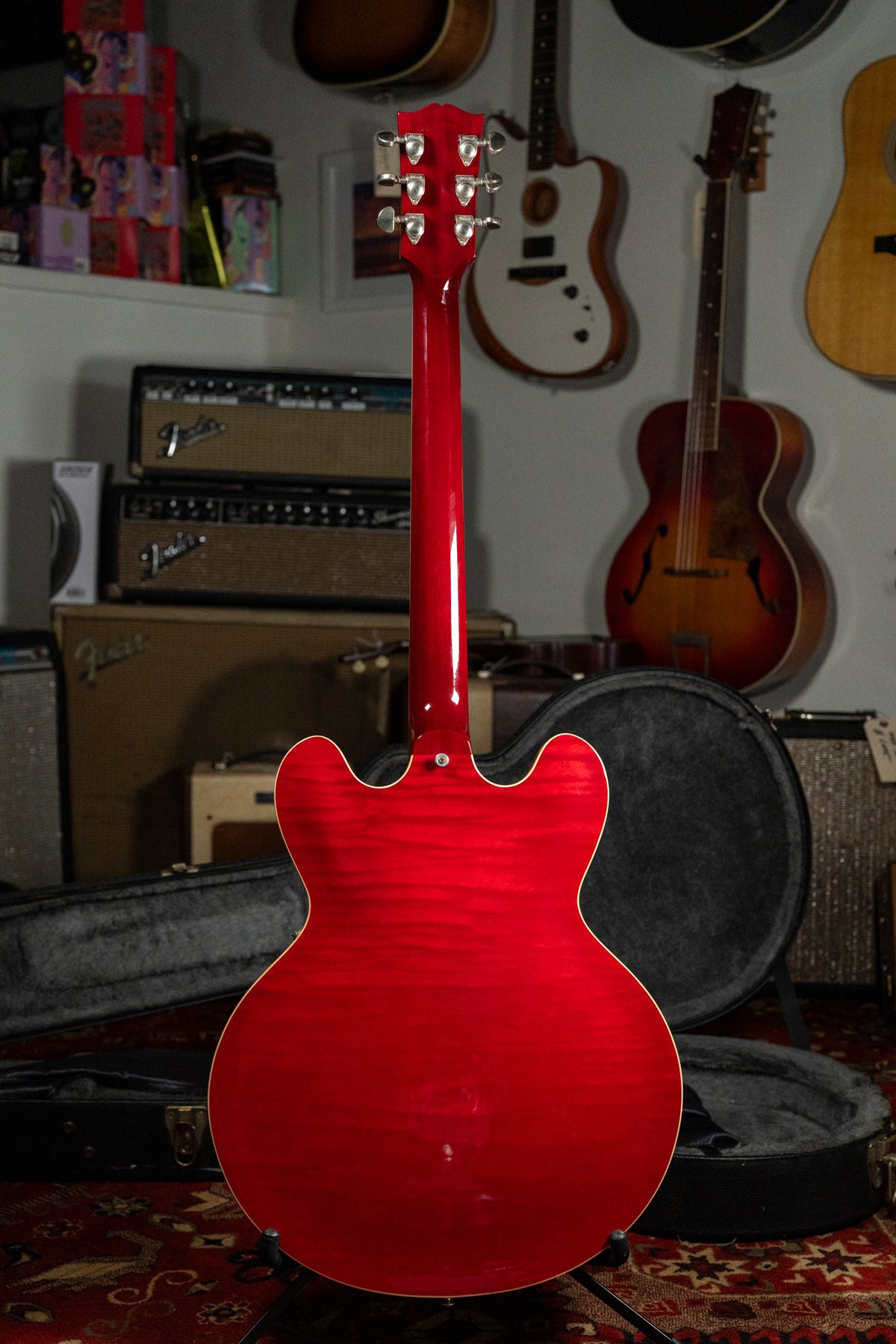 The back of a cherry red flamed maple guitar with a glossy finish, showing the neck, headstock with six tuners, and cream binding.