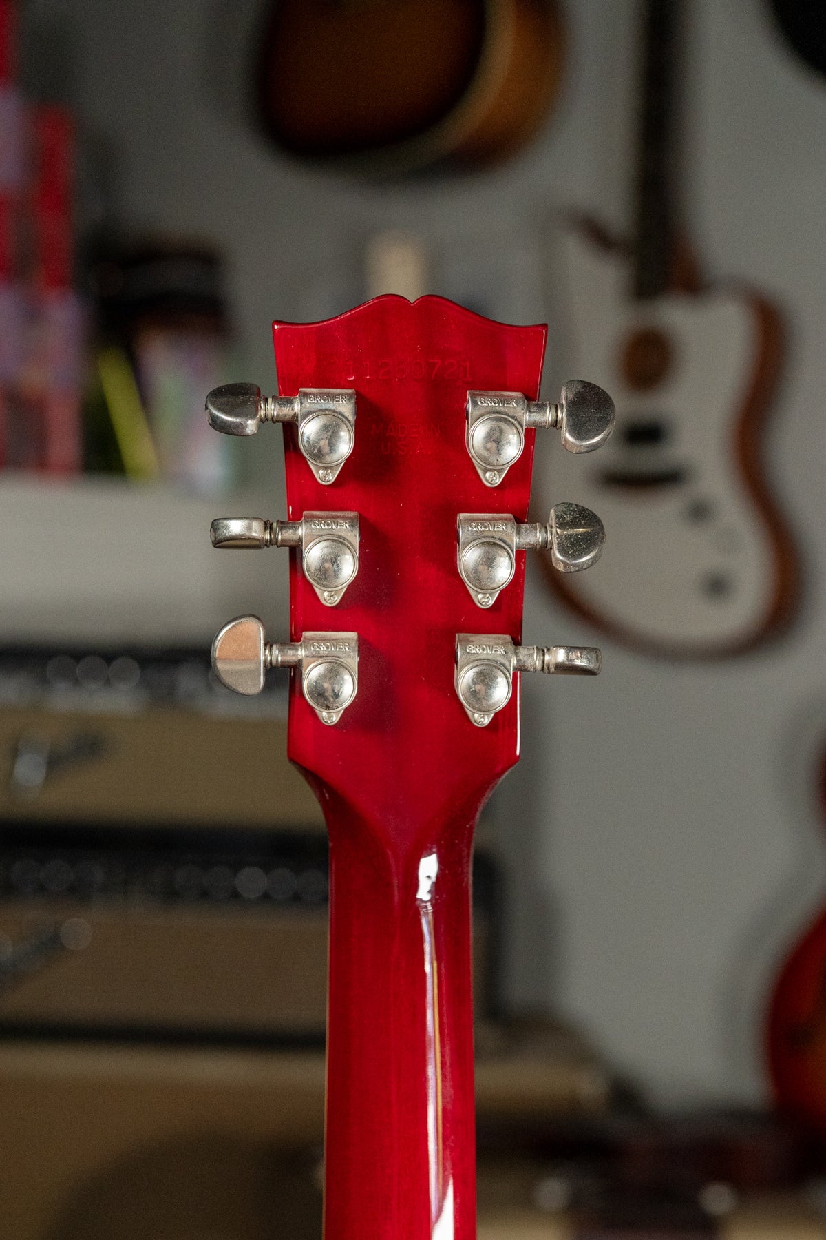 The guitar's cherry red headstock and neck are viewed from behind, showing six chrome Grover tuners and light finish wear.