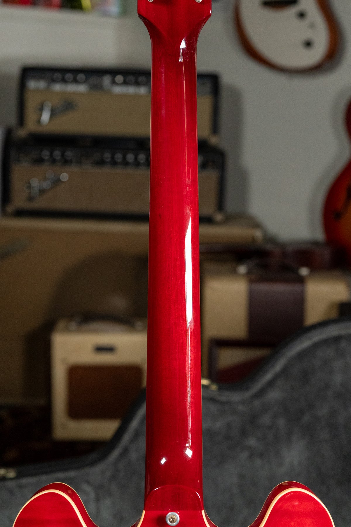 The back of a cherry red guitar neck with a glossy finish, showing some light wear and a strap button at the heel.