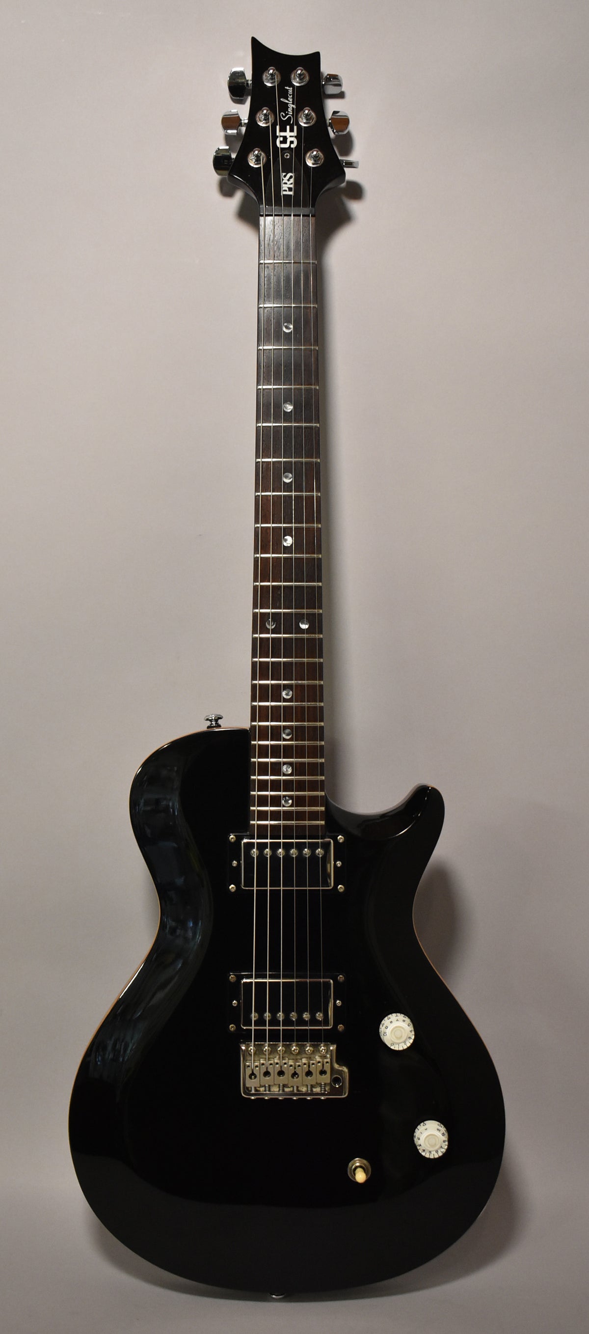 A black PRS SE Singlecut electric guitar with chrome hardware, two humbucker pickups, and two white control knobs.