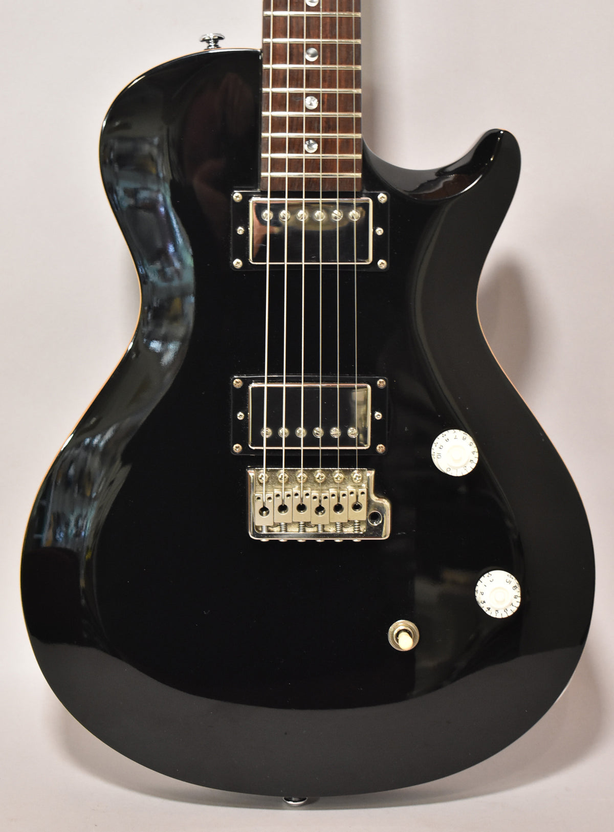Full-frame, glossy black singlecut electric guitar with two humbuckers, a tune-o-matic bridge, and two white control knobs.
