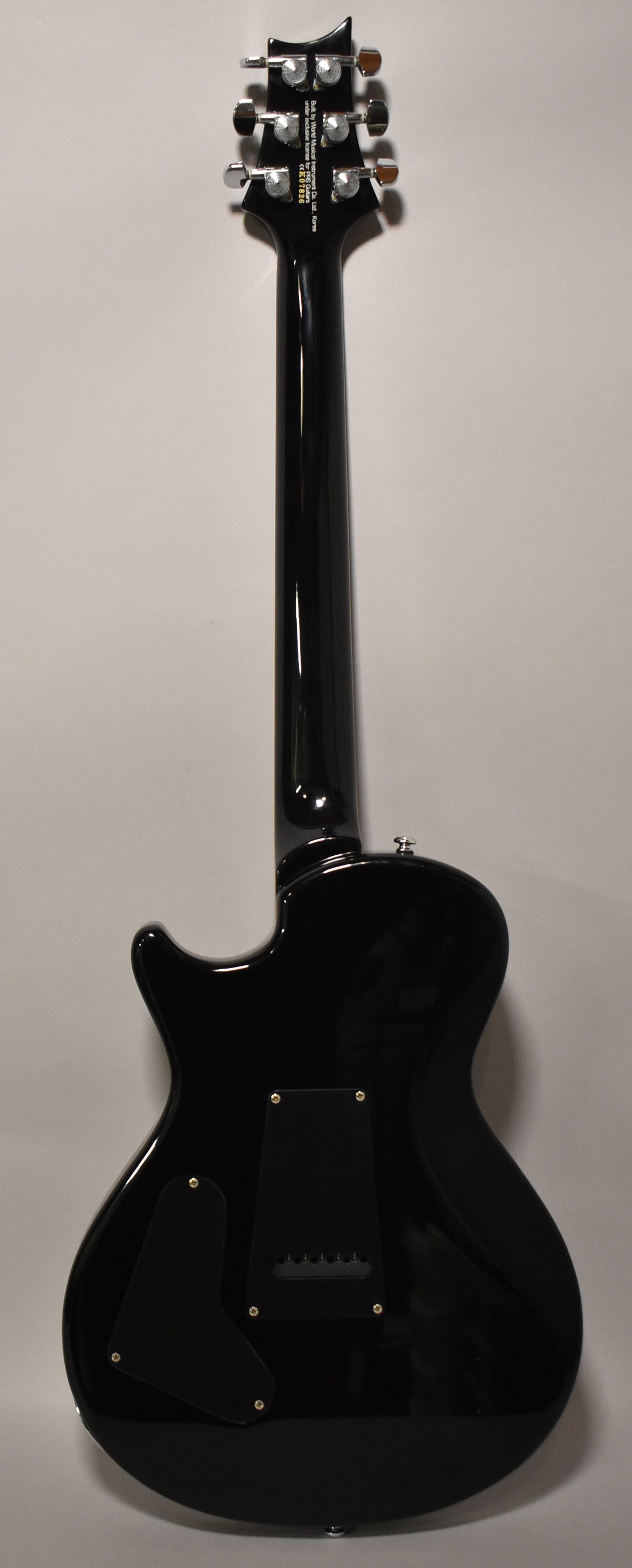 Full rear view of a glossy black electric guitar, showing the headstock with six chrome tuners and the back of the body with two control cavity covers.