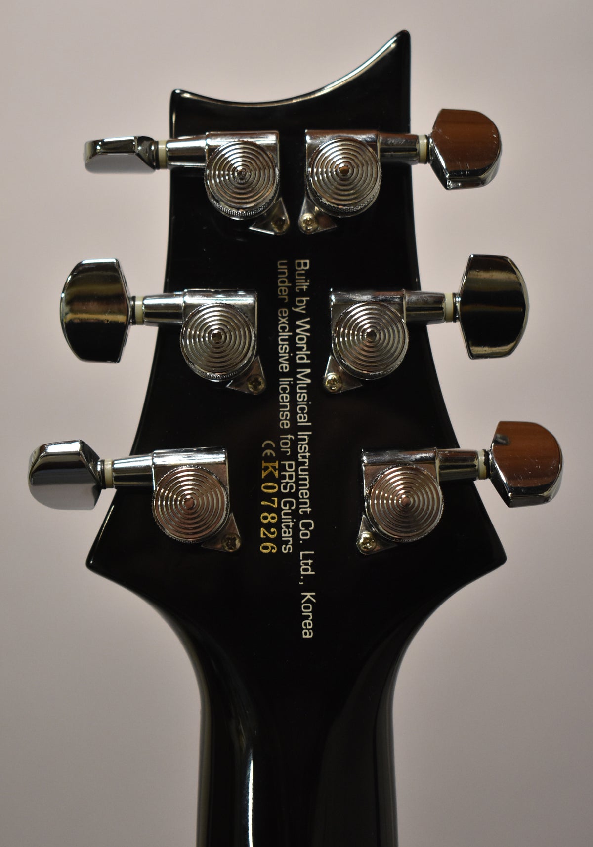 Rear view of the black headstock and top of the neck, showing six chrome tuners with ribbed buttons and some minor scuffs.