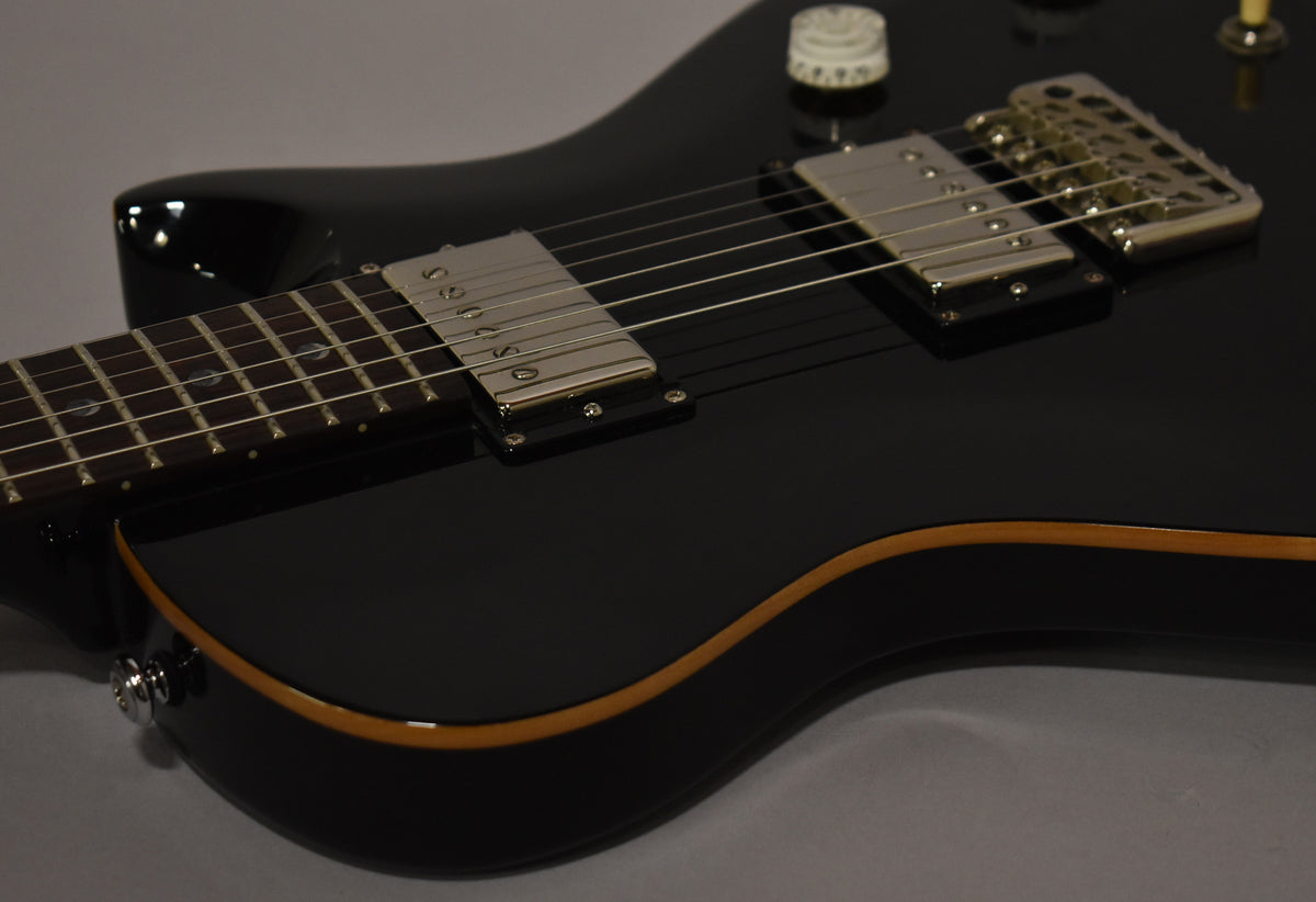 Close-up of the glossy black guitar body, showing the neck, two chrome humbuckers, a white control knob, and cream binding.