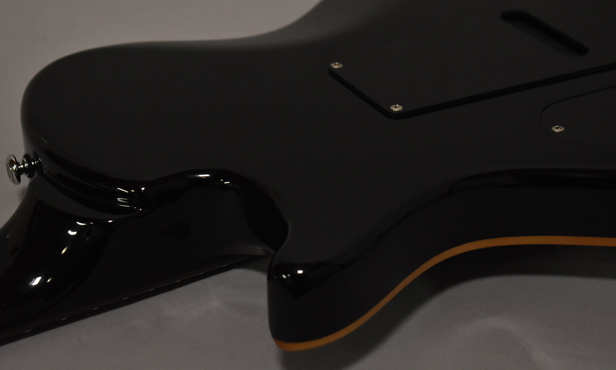 The guitar's glossy black body, with cream binding, is shown from the back, angled to reveal the neck joint and control cavity cover.
