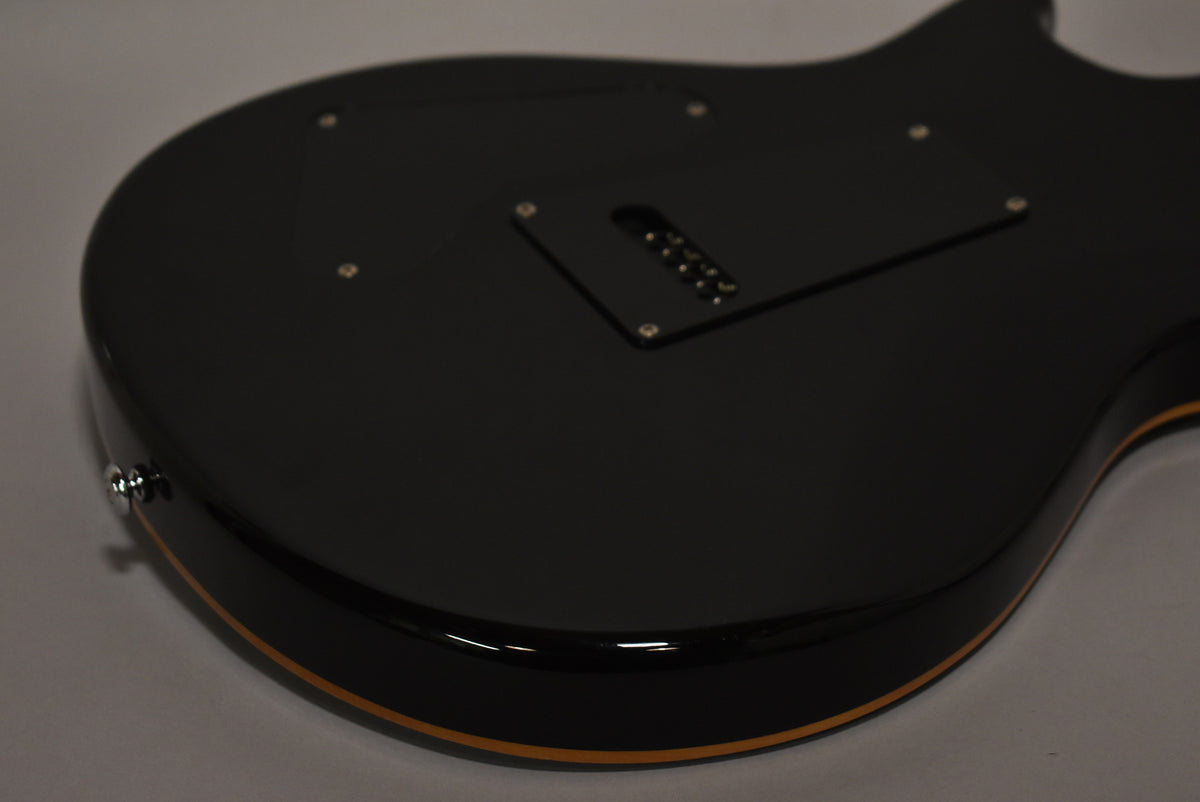 The guitar's glossy black back is angled, showing a tremolo spring cover, strap button, and a thin natural wood binding.