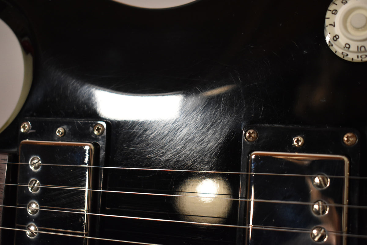 Close-up of the black guitar body with two chrome humbucker pickups, showing heavy pick scratches and a white volume knob.