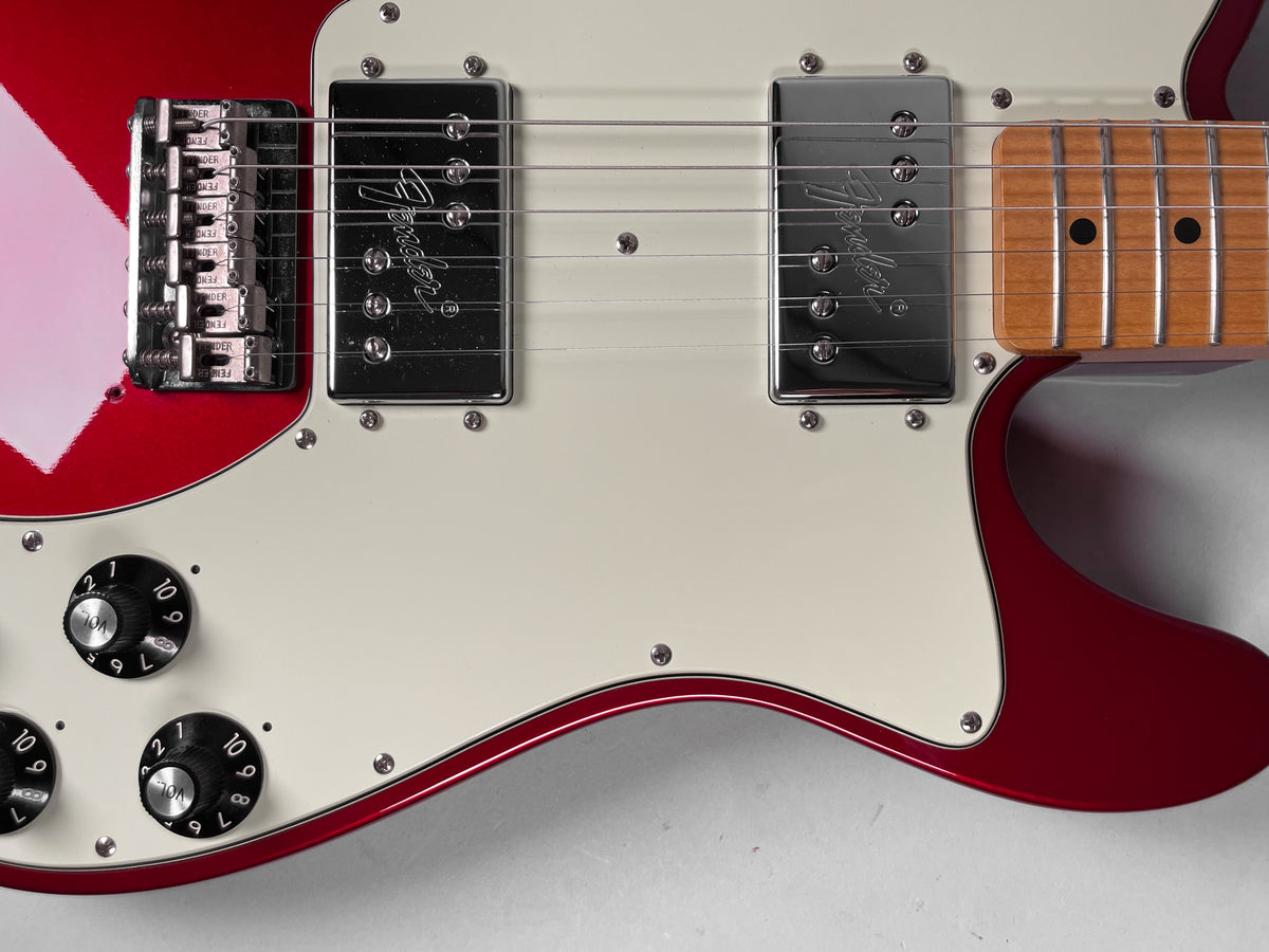 Close-up of the guitar's glossy candy apple red body, cream pickguard, chrome humbuckers, bridge, and four black control knobs.