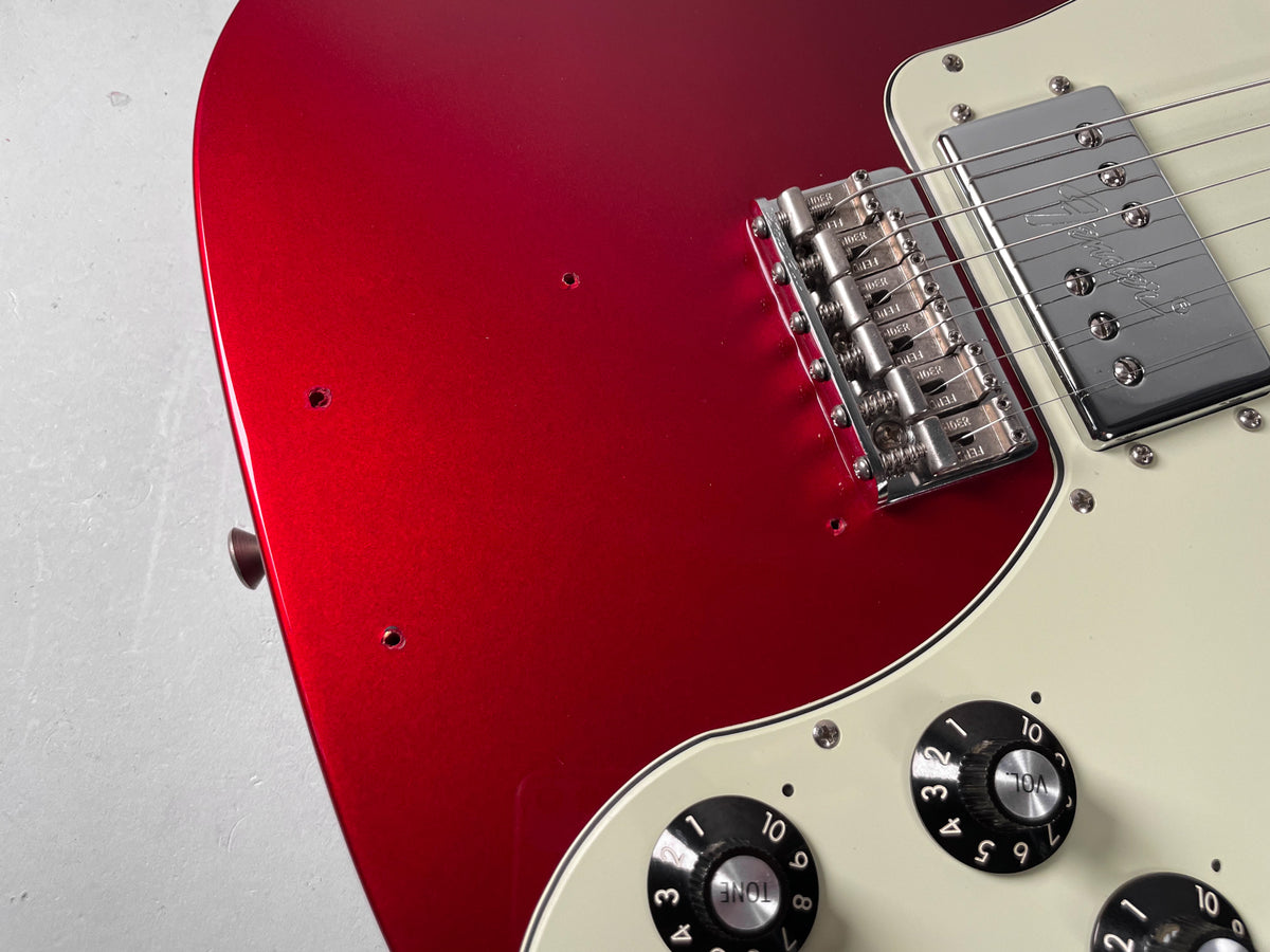 Close-up of a red guitar body with a cream pickguard, showing the bridge, a humbucker pickup, and three control knobs.