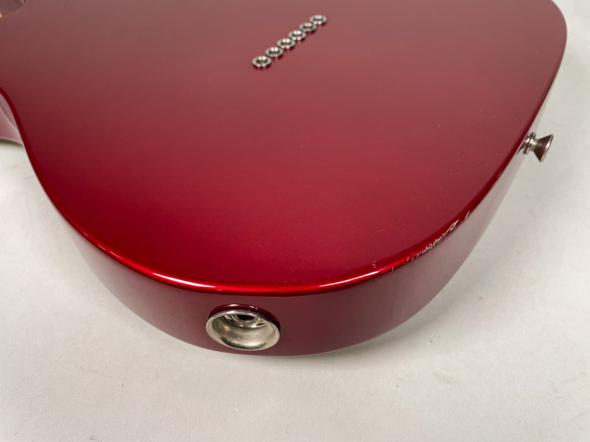 The candy apple red guitar body, viewed from the lower bout, shows a chrome output jack and strap button, with a few scratches.