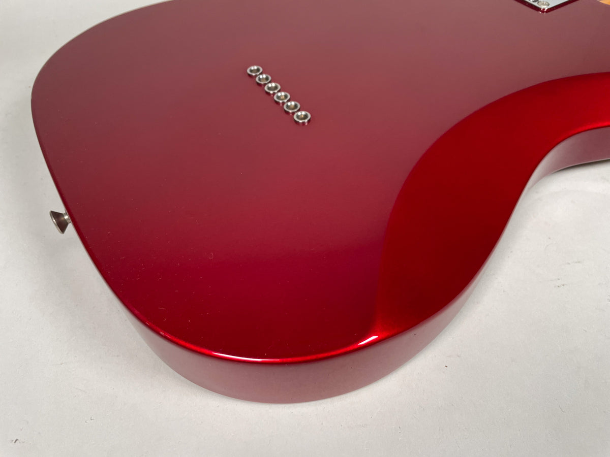 The guitar's candy apple red body, with a glossy finish, is viewed from the back, showing six string-through-body ferrules and a strap button.