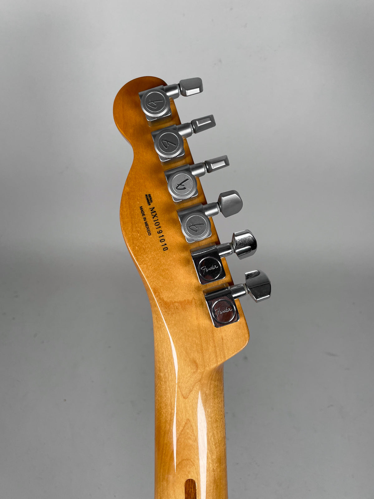 The guitar's glossy amber headstock and neck are viewed from behind, showing six chrome tuners with square buttons.