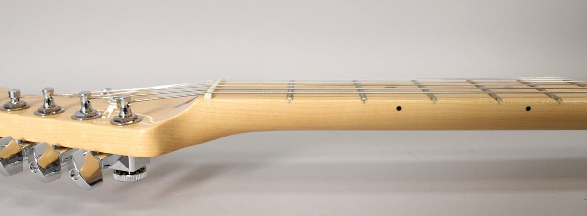 The guitar's light maple neck and headstock are viewed from the side, showing six chrome tuners and dark fretboard dots.