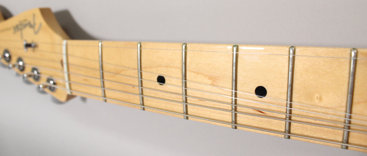Close-up of the maple fretboard and headstock, showing the first few frets, dot inlays, and six chrome tuners.