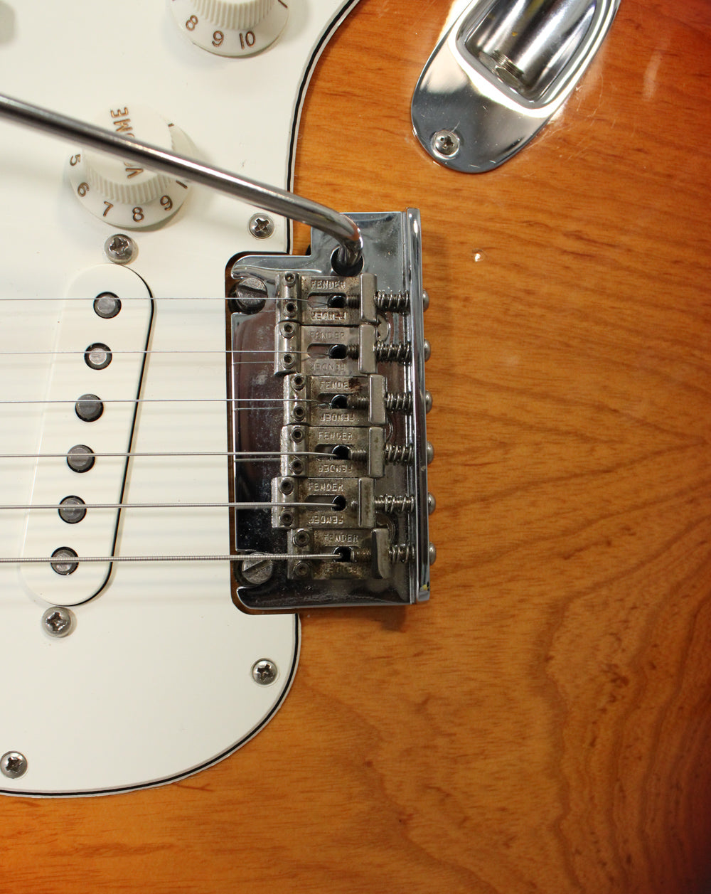 Close-up of the Sienna Burst body, showing the chrome tremolo bridge with whammy bar, white pickguard, and two cream control knobs.