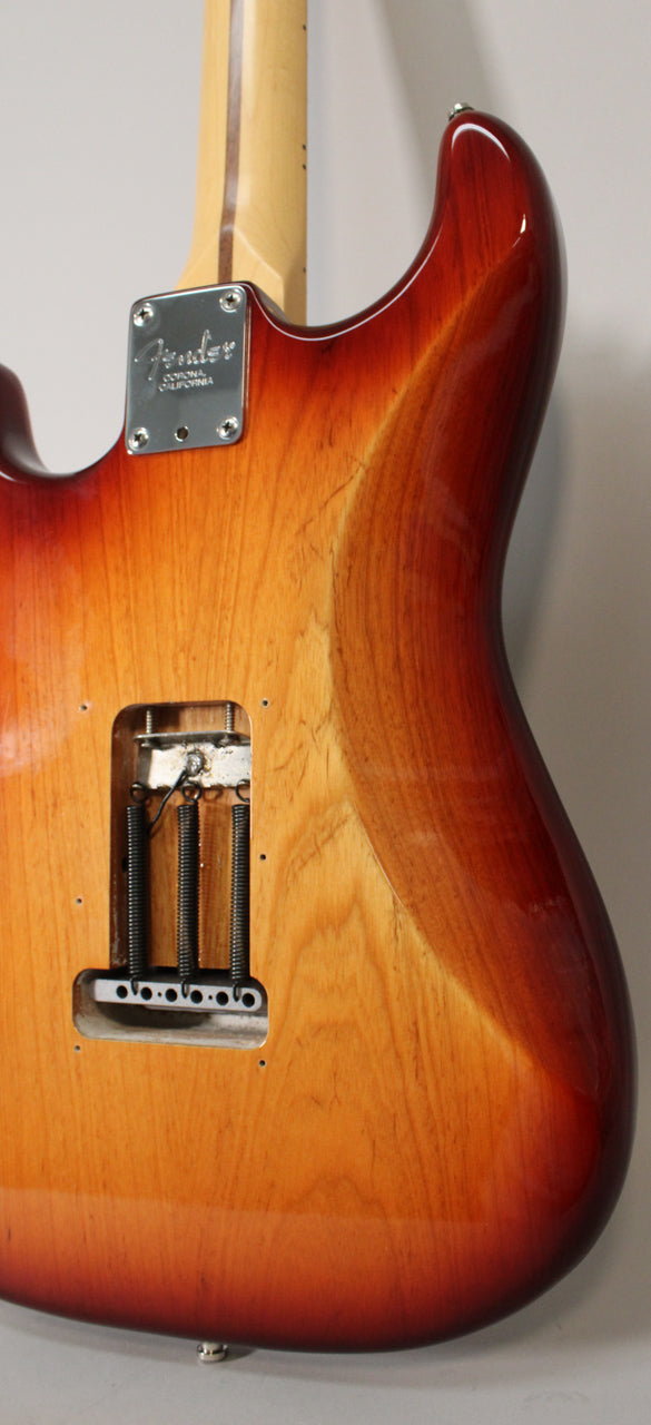 Rear view of a Sienna Burst Stratocaster body, showing the tremolo spring cavity, neck plate, and some light scratches on the finish.