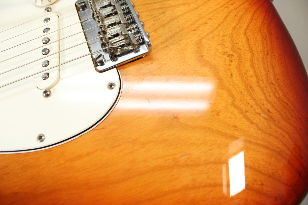 Close-up of the Sienna Burst body, showing the lower horn, white pickguard, middle pickup, and chrome tremolo bridge with light play wear.