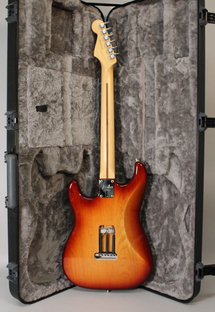 Full rear view of a Sienna Burst Stratocaster in its open hard shell case, showing the maple neck, headstock, and tremolo cavity.
