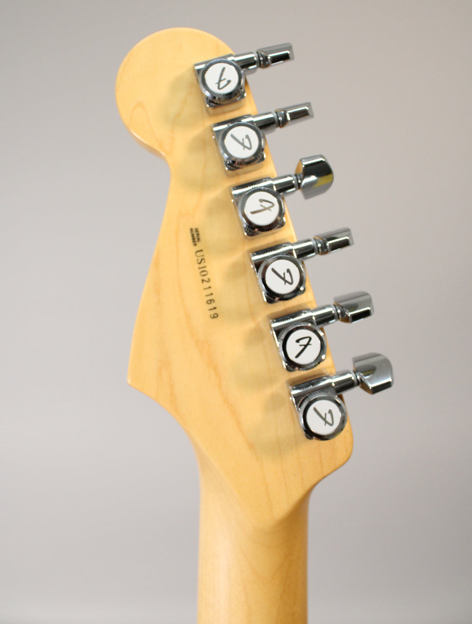 Rear view of the maple headstock and neck, showing six chrome tuners with white buttons and a visible serial number.