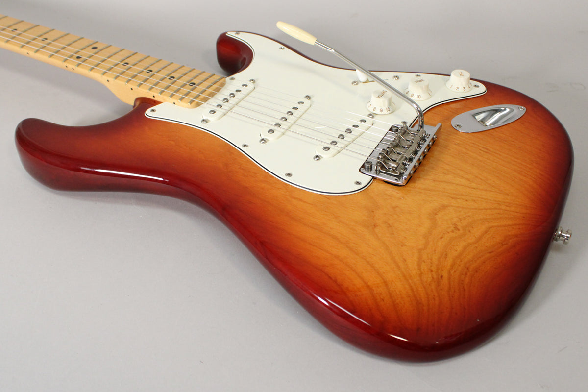 The Sienna Burst Stratocaster is angled from the upper left, showing the body, white pickguard, three single-coil pickups, and tremolo bridge.