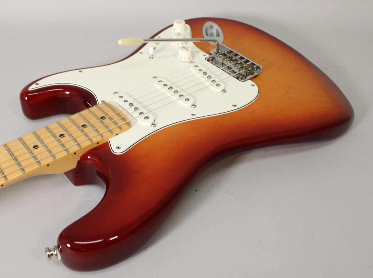 The guitar's Sienna Burst body, white pickguard, and maple neck are shown from above, angled to the right.