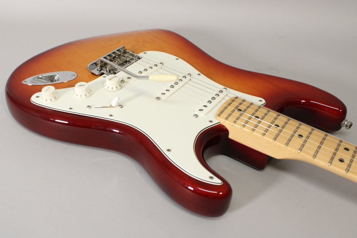 A Sienna Burst Stratocaster, angled from the lower bout, showing the glossy finish, white pickguard, and maple fretboard.