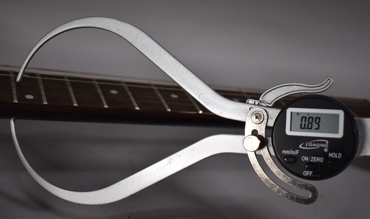 A digital caliper measures the fret height on the dark rosewood fretboard, displaying "0.89" on its screen.