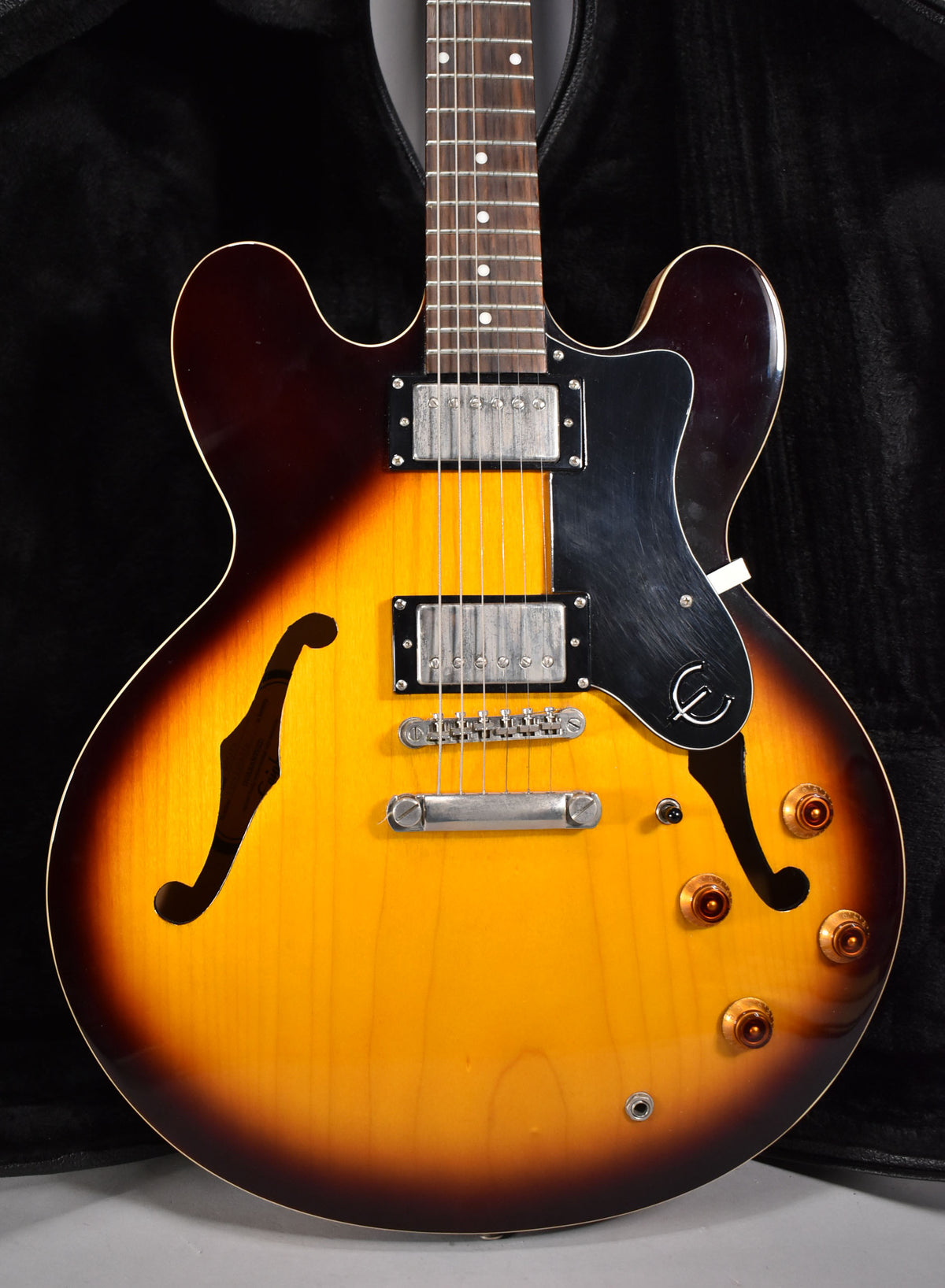 Full-frame, front view of a sunburst semi-hollowbody electric guitar with f-holes, two humbuckers, and four amber control knobs.