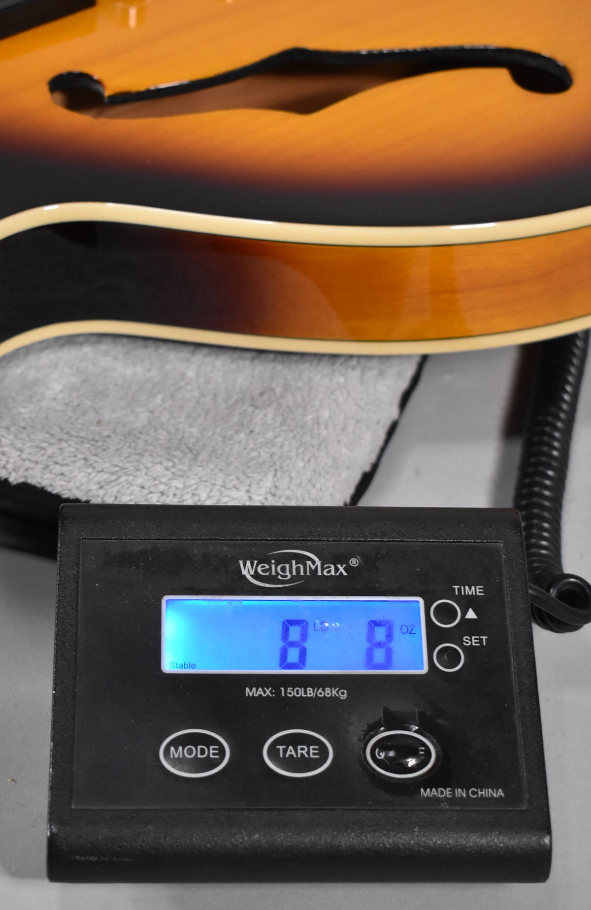 The guitar's sunburst body, with f-holes and cream binding, rests on a scale displaying "8 LB 8 OZ" in blue.