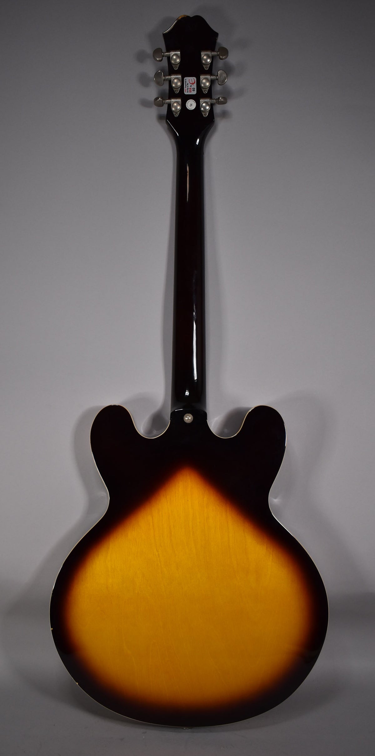 Full rear view of a sunburst semi-hollow guitar, showing the dark brown neck, headstock with six tuners, and light wear on the body.