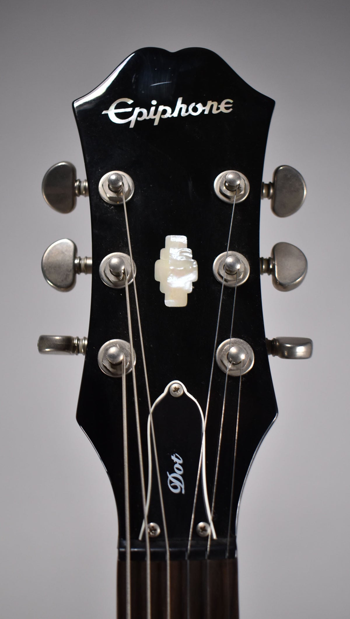 Close-up of the black headstock, showing six silver tuners, a mother-of-pearl inlay, and light scratches on the glossy finish.