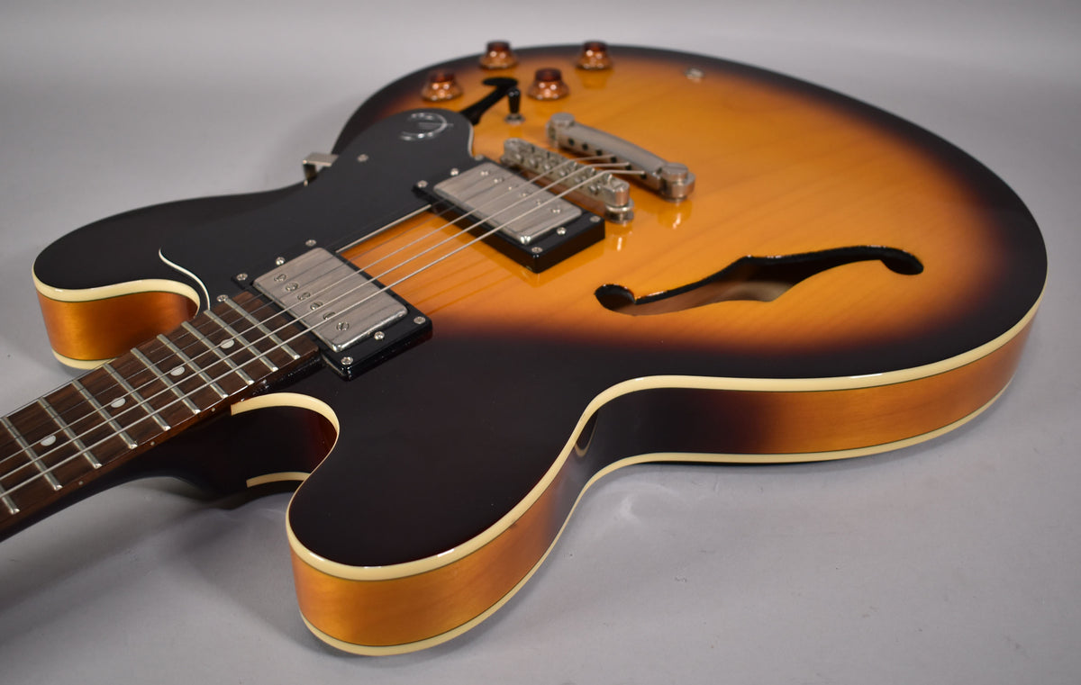 The sunburst semi-hollowbody guitar is angled from the lower bout, showing the neck, black pickguard, and f-holes.