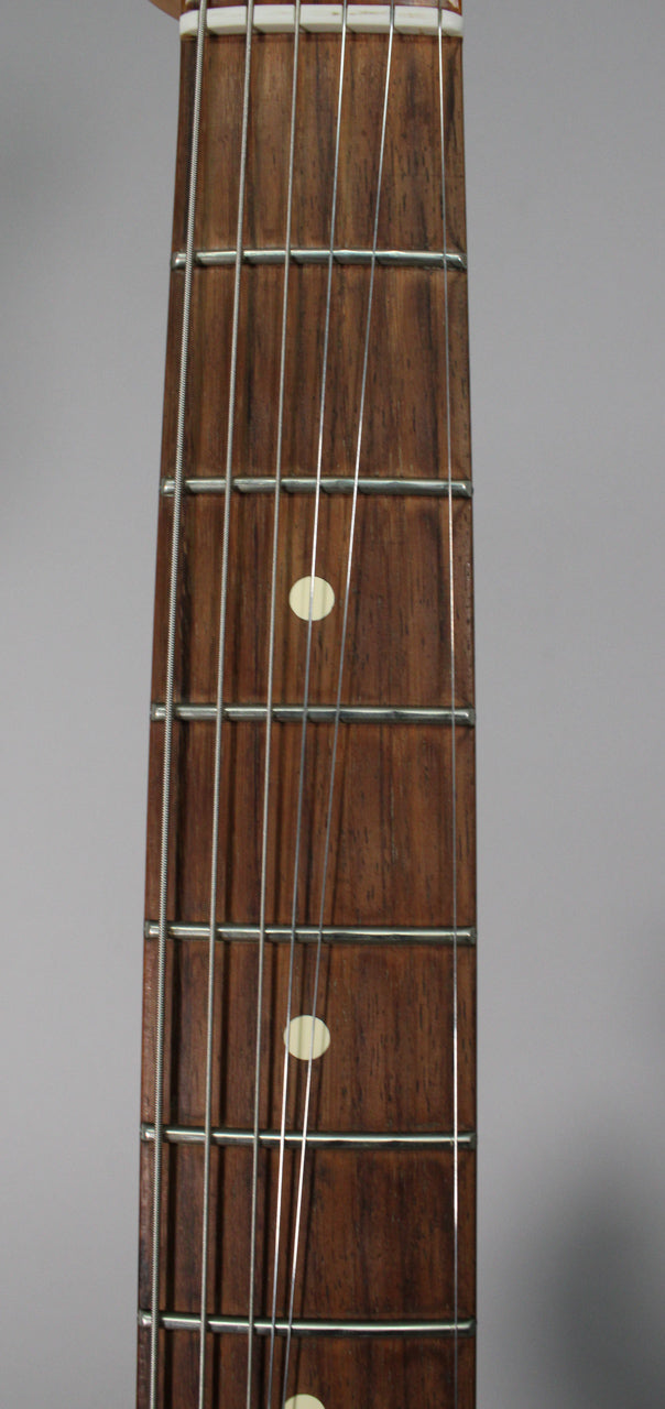 Close-up of the dark rosewood fretboard with six strings, silver frets, and three cream dot inlays visible.
