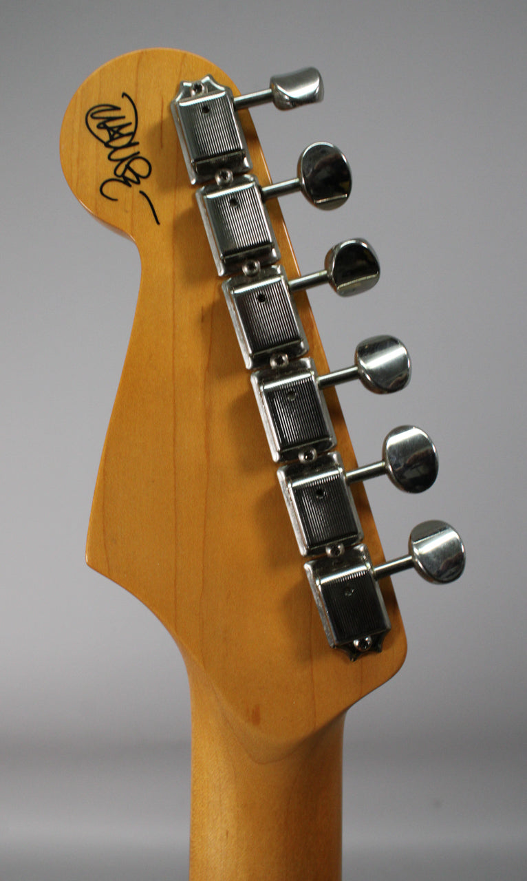 Close-up of the light brown maple headstock and neck, showing six chrome tuners and a black signature on the headstock.