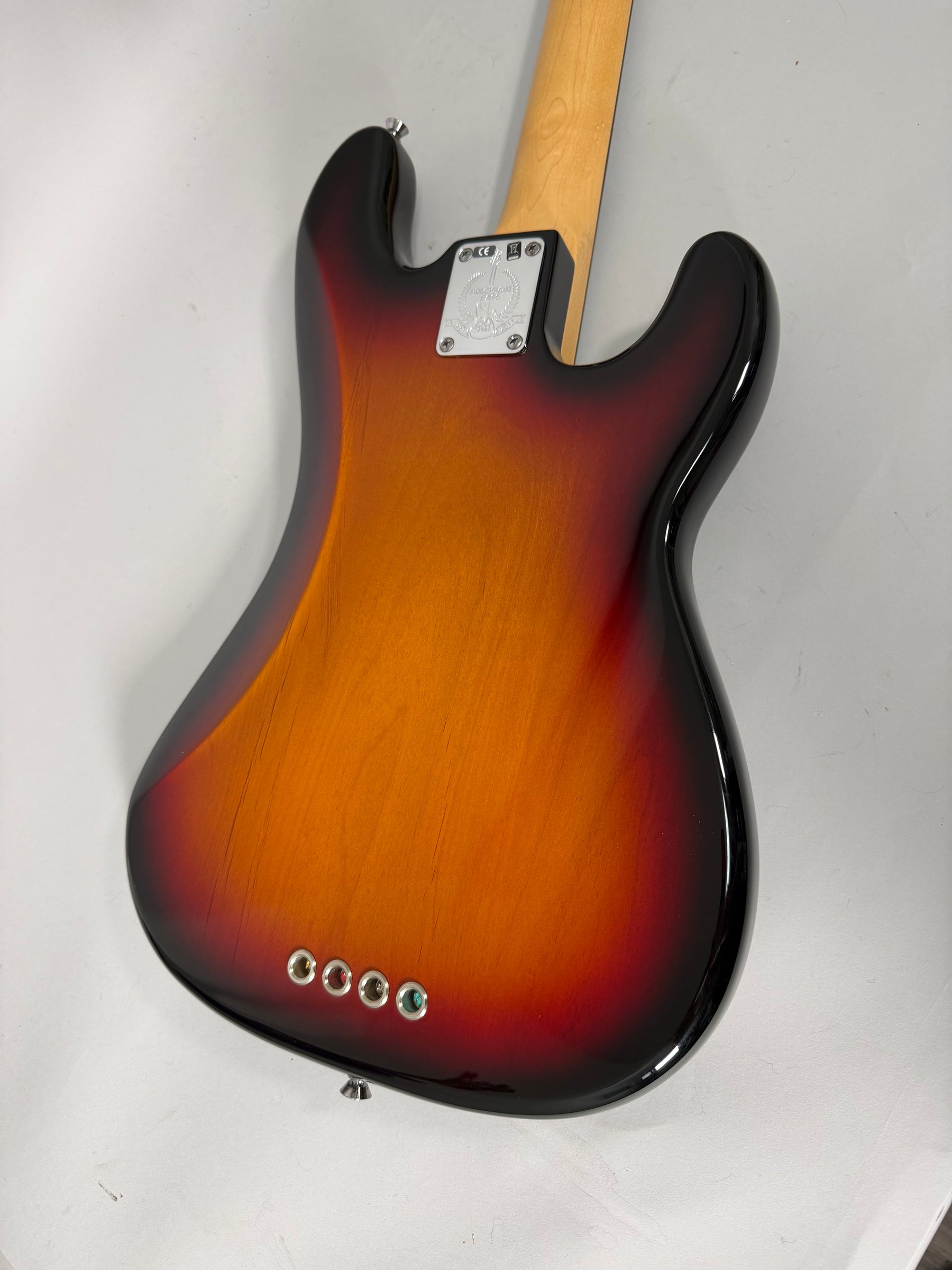 The bass's sunburst body, with a visible wood grain, is seen from the back, showing the neck plate and four string ferrules.
