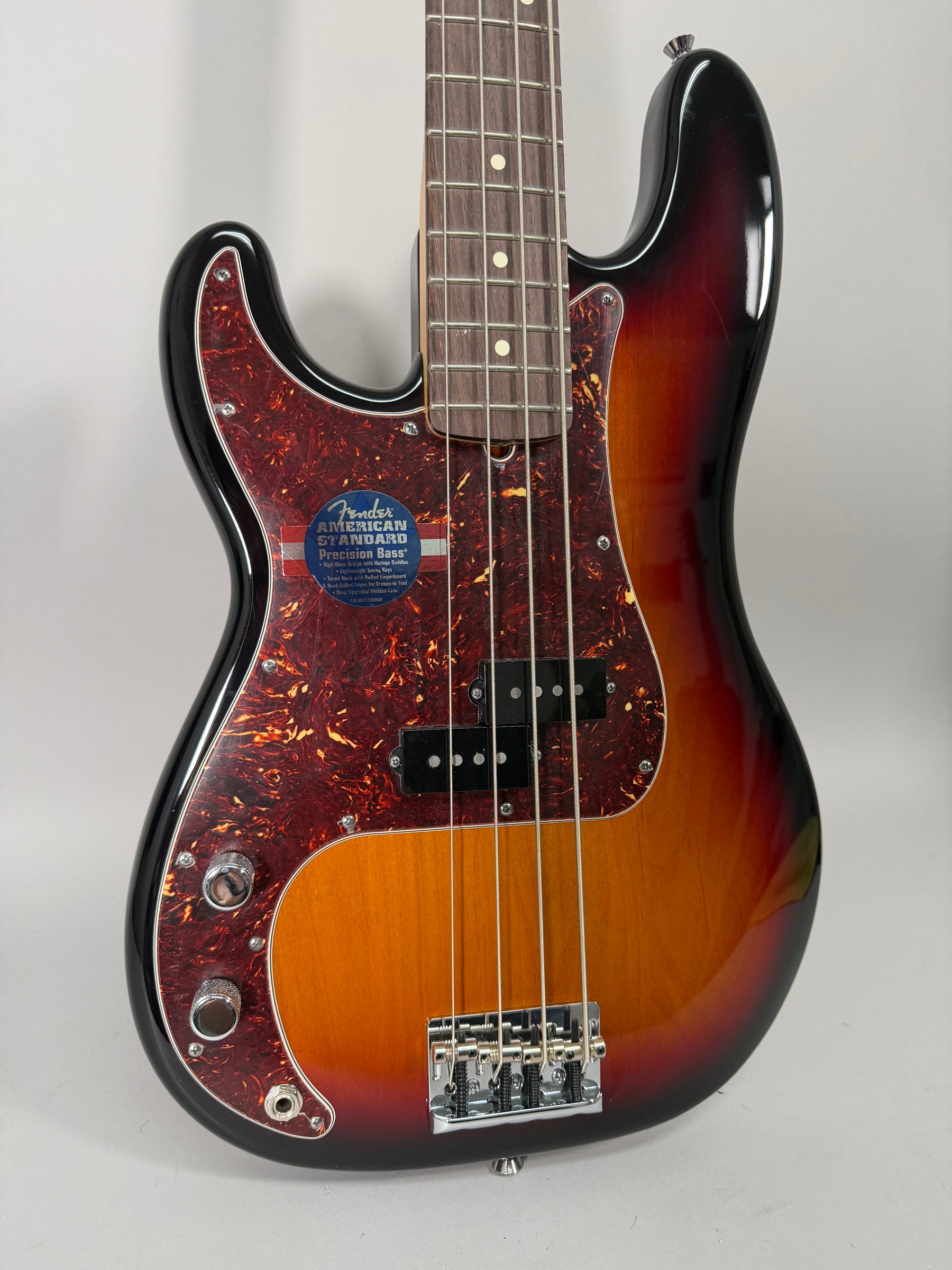 A sunburst left-handed Fender Precision Bass with a tortoiseshell pickguard and a blue "Fender American Standard Precision Bass" sticker.