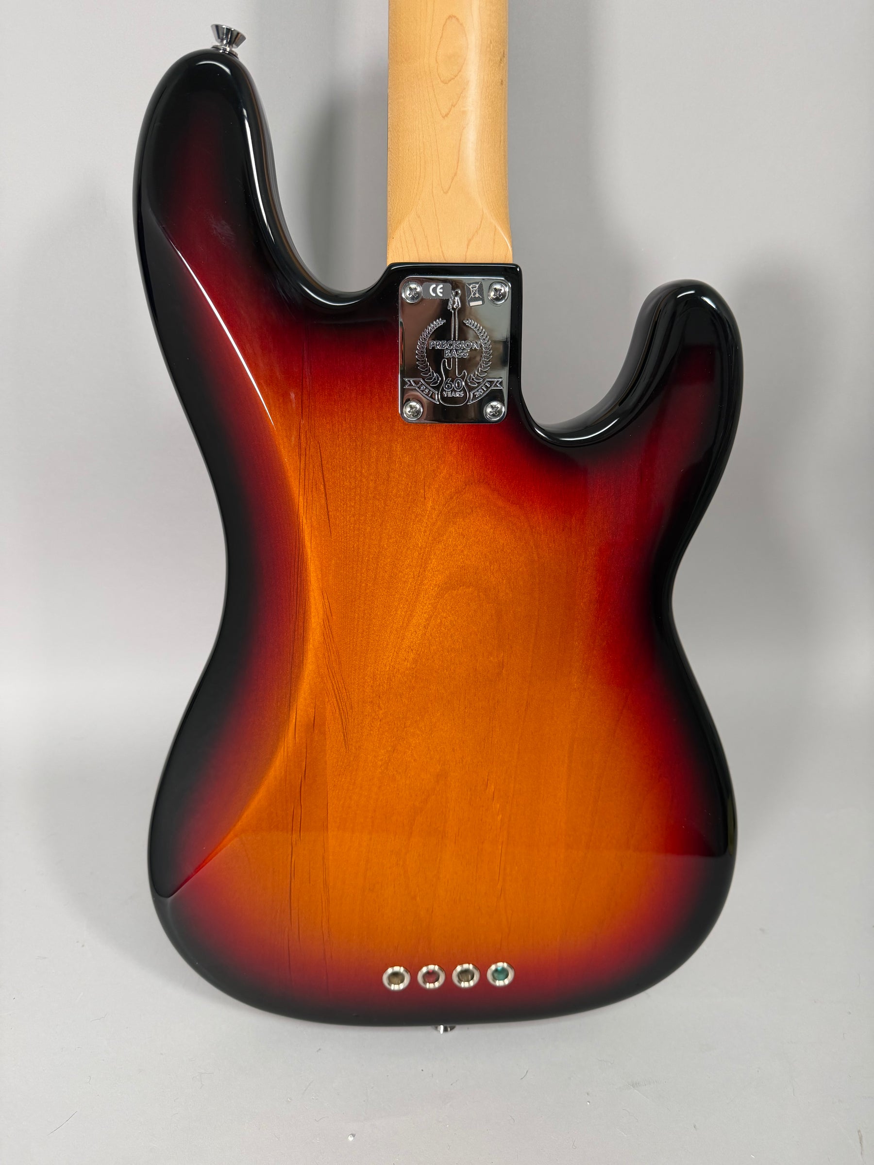 The bass's sunburst back shows light scratches, a chrome neck plate, and four string ferrules near the bottom edge.