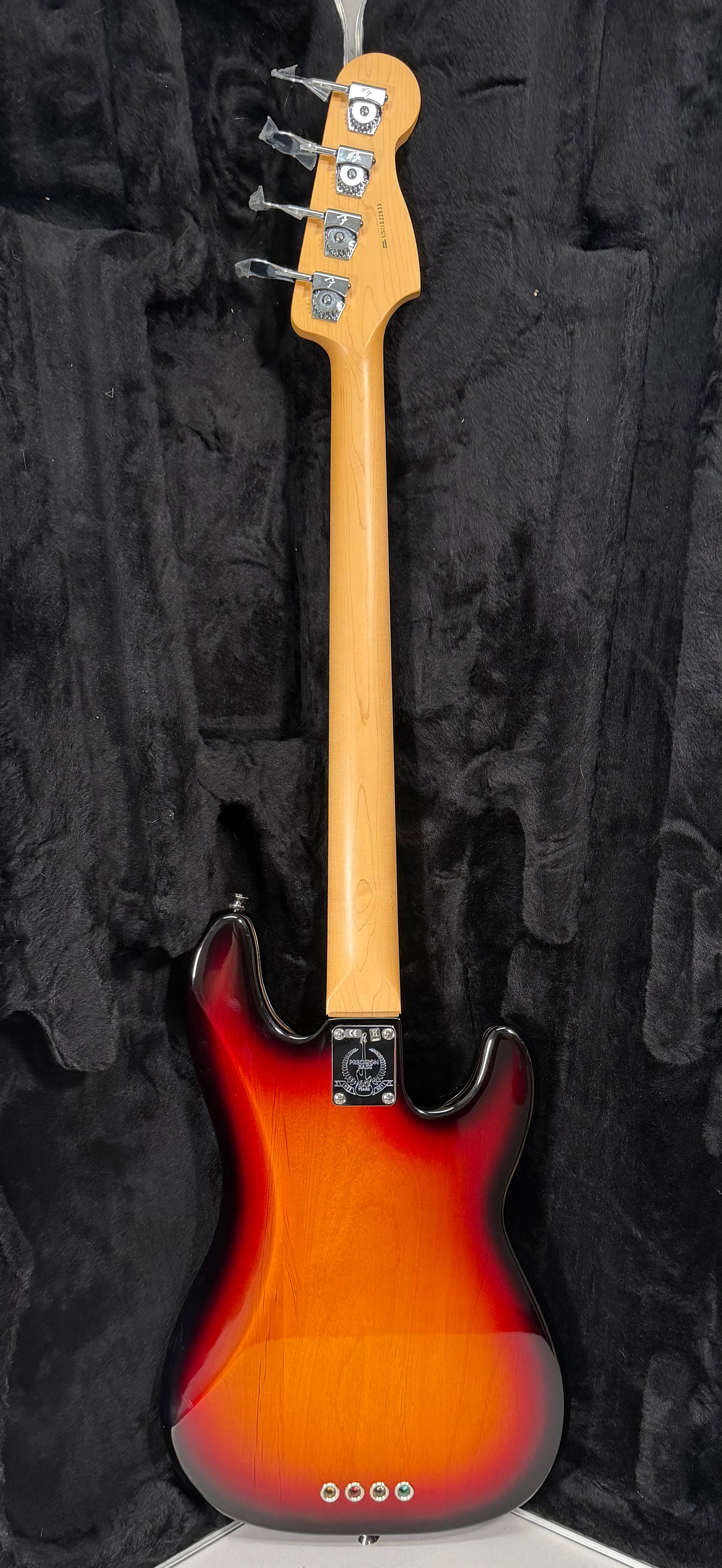 Full rear view of a sunburst bass, showing the light maple neck and headstock with four chrome tuners, and a small ding on the body.
