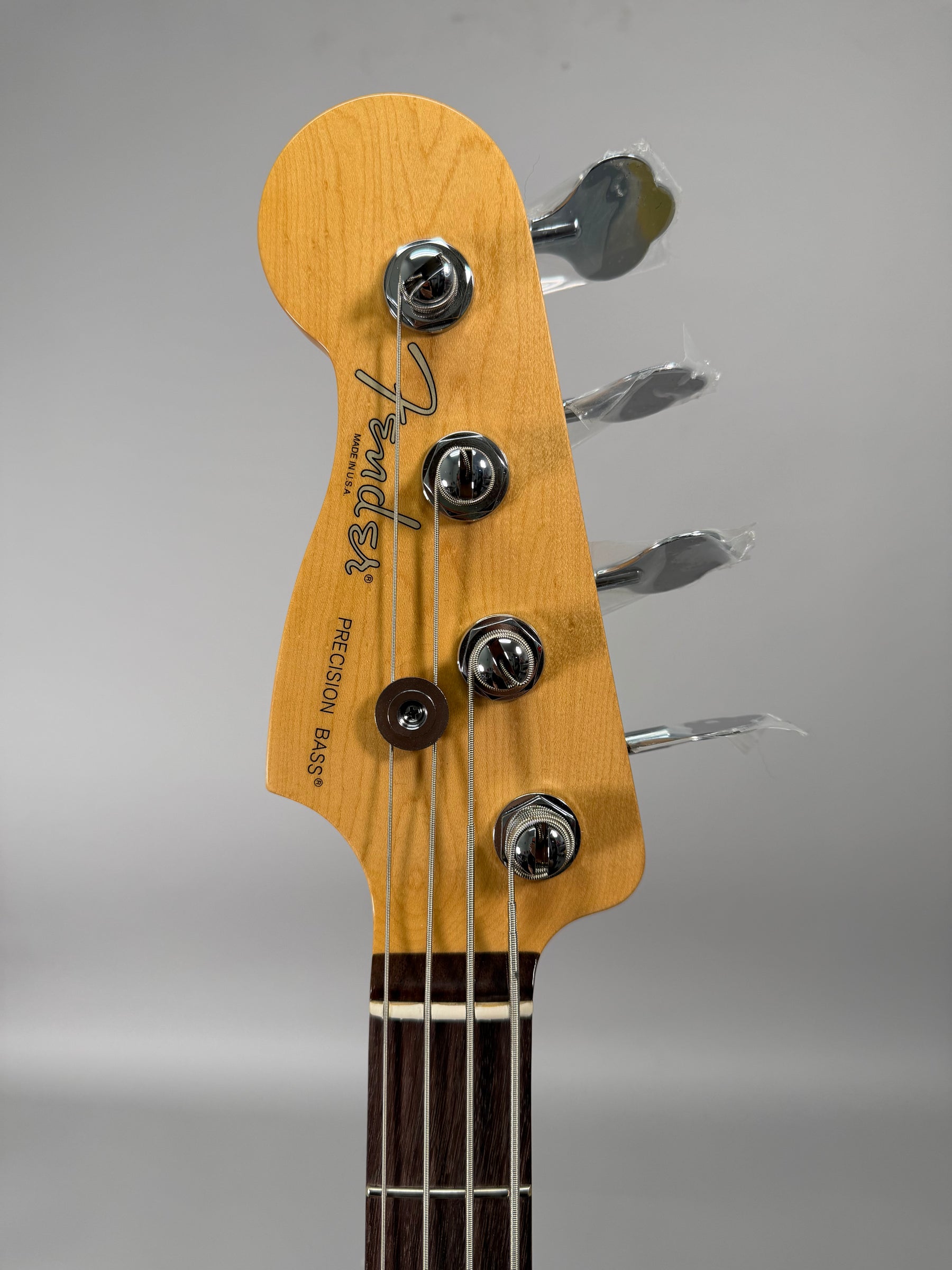 Close-up of the light wood headstock and dark fretboard, with four chrome tuners, three still wrapped in plastic.