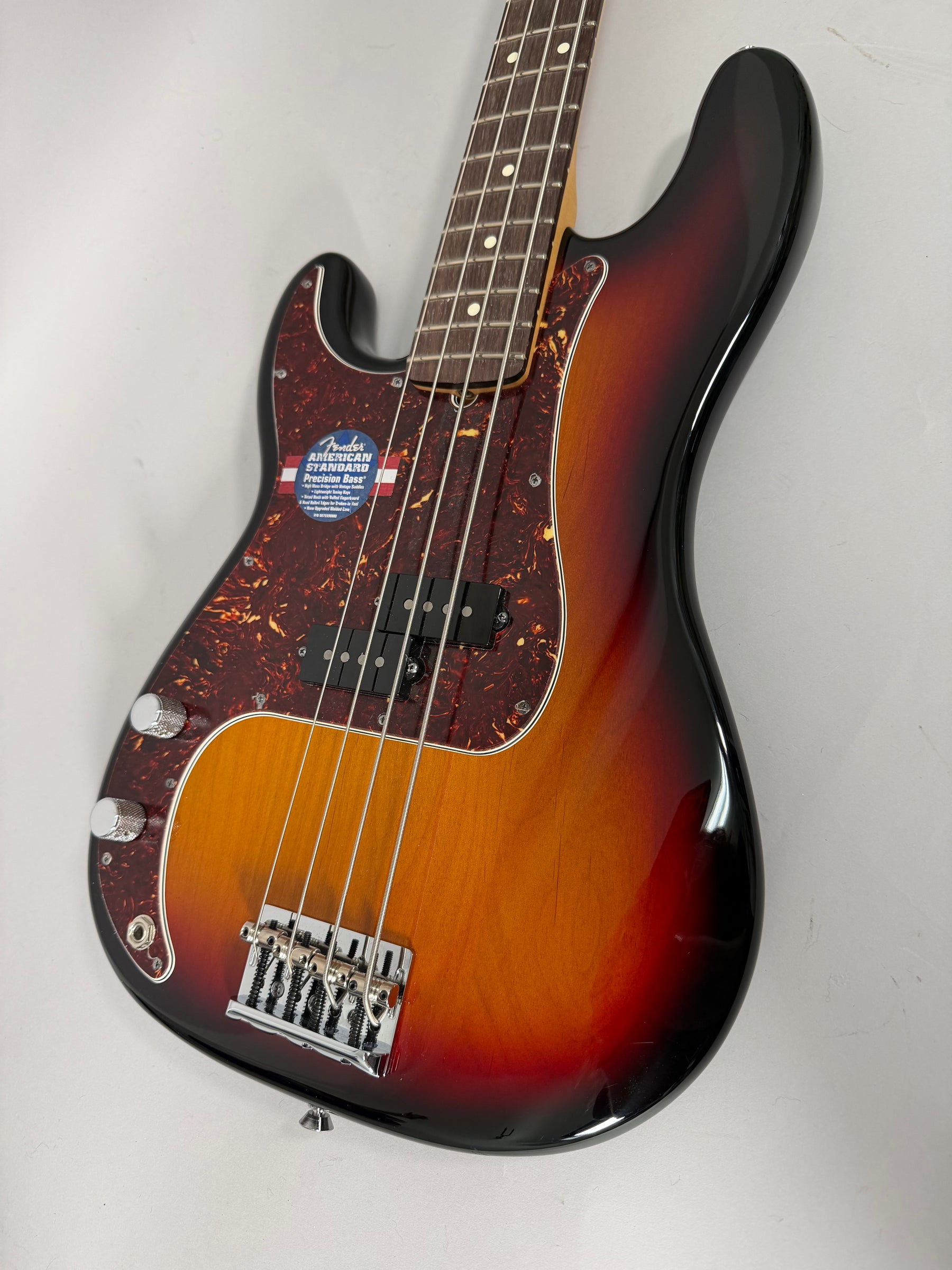 The sunburst bass is angled from the headstock, showing the dark tortoiseshell pickguard, split pickup, and chrome bridge.